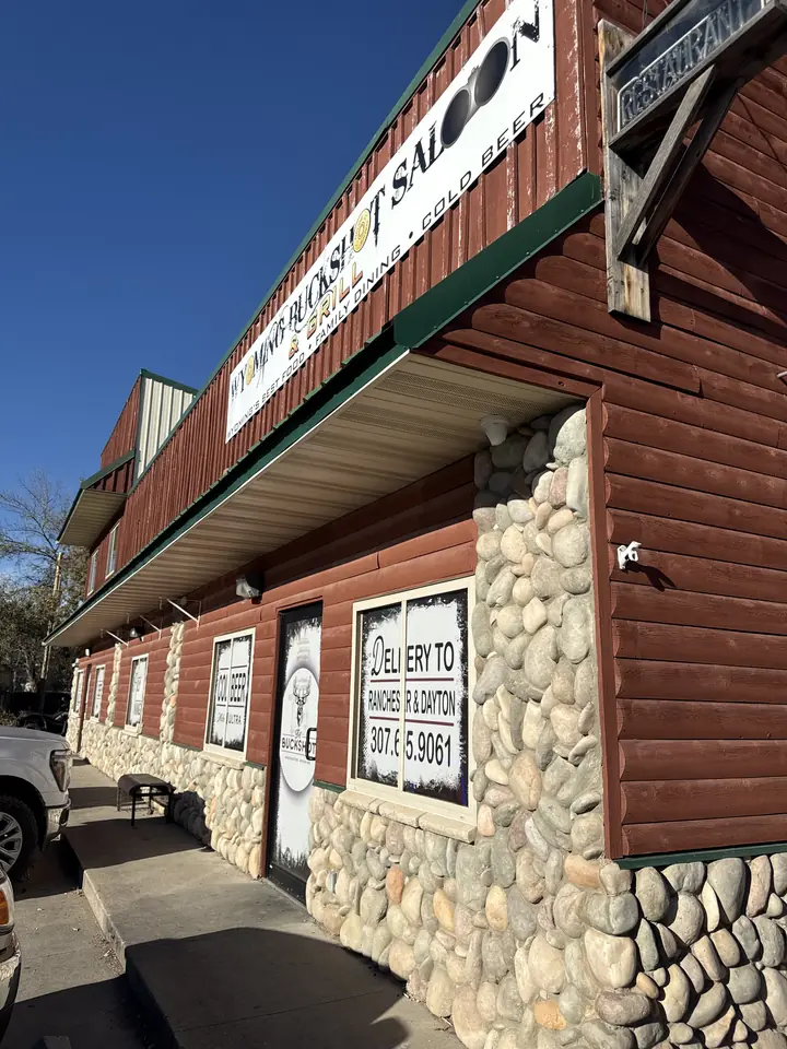 Front entrance of Wyoming Buckshot Saloon & Grill, a red log-sided building with river-rock walls and the Buckshot sign above the door.